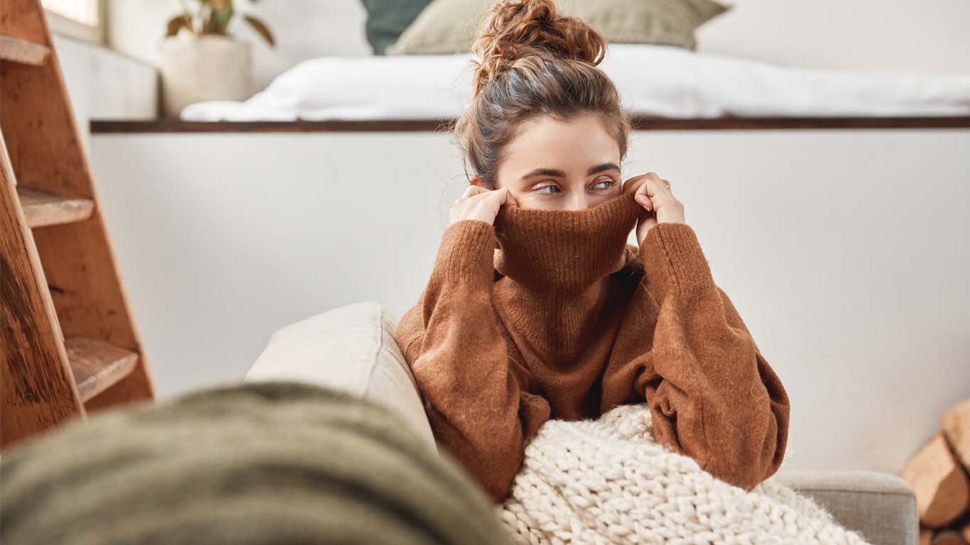 Vrouw met knuffeldeken verbergt haar gezicht onder haar coltrui.